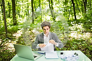 Young handsome business man at work table office with laptop in green forest tear work papers. Business concept