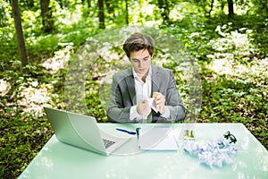 Young handsome business man at work table office with laptop in green forest tear work papers. Business concept