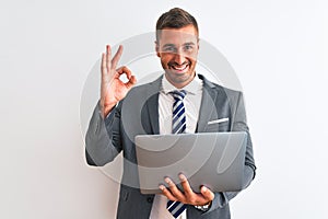 Young handsome business man working using computer laptop over isolated background doing ok sign with fingers, excellent symbol