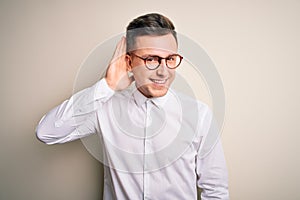 Young handsome business mas wearing glasses and elegant shirt over isolated background smiling with hand over ear listening an