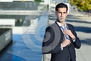 Young handsome businessman adjusting a tie in urban background