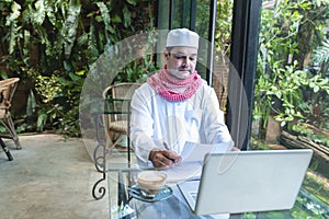 Young handsome businessman arab muslims in coffee shop wearing hijab dressed look at paper file with laptop on table