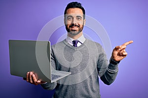 Young handsome businessman with beard working using laptop over purple background very happy pointing with hand and finger to the