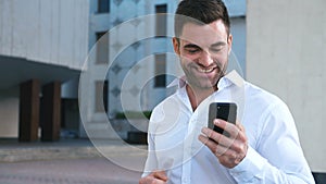 Young Handsome Businessman Celebrating Success while Reading Message in Smartphone near office building. Business