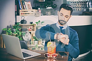 Young handsome businessman checking time on his wrist watch at a cafe.