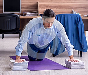 Young handsome businessman doing exercises at workplace