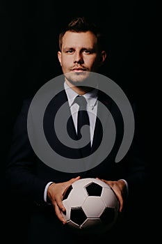 Young handsome businessman holding a football on black background studio.