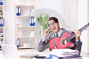 The young handsome businessman playing guitar in the office