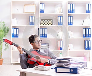 Young handsome businessman playing guitar in the office