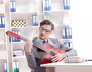 Young handsome businessman playing guitar in the office