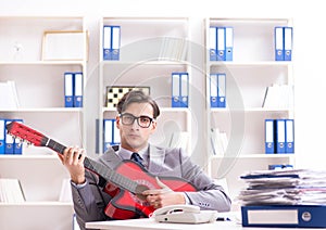 Young handsome businessman playing guitar in the office