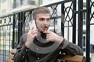 Young handsome businessman sits on bench and speaks on cell phone