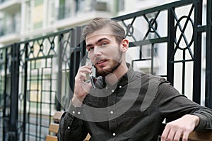 Young handsome businessman sits on bench and speaks on mobile phone