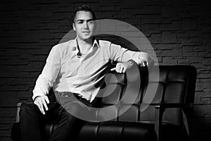 Young handsome businessman sitting with confidence on leather couch thinking