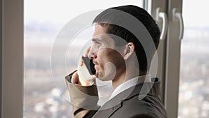 Young handsome businessman talking mobile phone near the panoramic window. slow motion. 3840x2160