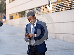 Young handsome businessman using mobile phone app sending message outside office in urban city