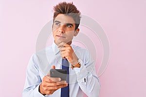 Young handsome businessman using smartphone standing over isolated pink background serious face thinking about question, very