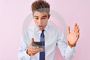 Young handsome businessman using smartphone standing over isolated pink background very happy and excited, winner expression