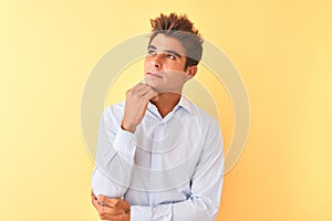 Young handsome businessman wearing elegant shirt over isolated yellow background with hand on chin thinking about question,