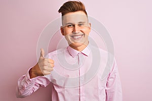 Young handsome businessman wearing elegant shirt standing over isolated pink background doing happy thumbs up gesture with hand