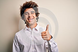 Young handsome businessman wearing elegant shirt standing over isolated white background doing happy thumbs up gesture with hand