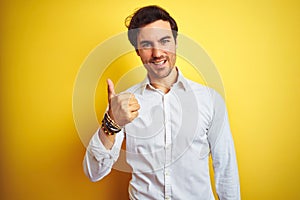Young handsome businessman wearing elegant shirt standing over isolated yellow background doing happy thumbs up gesture with hand