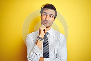 Young handsome businessman wearing elegant shirt and tie over isolated yellow background with hand on chin thinking about