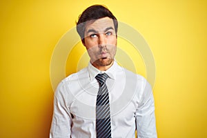 Young handsome businessman wearing elegant shirt and tie over isolated yellow background making fish face with lips, crazy and