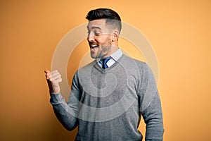 Young handsome businessman wearing elegant sweater and tie over yellow background smiling with happy face looking and pointing to