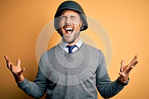 Young handsome businessman wearing military helmet over isolated yellow background crazy and mad shouting and yelling with