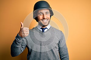 Young handsome businessman wearing military helmet over isolated yellow background doing happy thumbs up gesture with hand