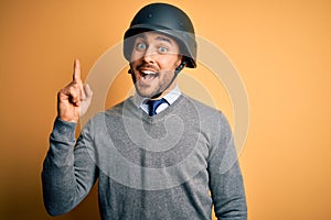 Young handsome businessman wearing military helmet over isolated yellow background pointing finger up with successful idea