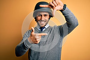 Young handsome businessman wearing military helmet over isolated yellow background smiling making frame with hands and fingers