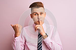 Young handsome businessman wearing shirt and tie standing over isolated pink background asking to be quiet with finger on lips