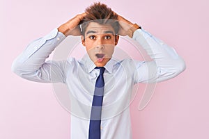 Young handsome businessman wearing shirt and tie standing over isolated pink background Crazy and scared with hands on head,