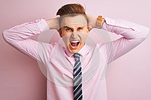 Young handsome businessman wearing shirt and tie standing over isolated pink background Crazy and scared with hands on head,