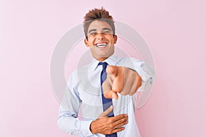 Young handsome businessman wearing shirt and tie standing over isolated pink background laughing at you, pointing finger to the