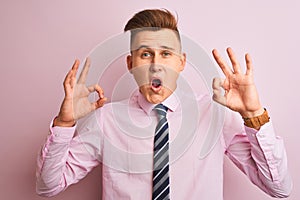 Young handsome businessman wearing shirt and tie standing over isolated pink background looking surprised and shocked doing ok