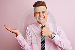 Young handsome businessman wearing shirt and tie standing over isolated pink background Showing palm hand and doing ok gesture