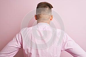 Young handsome businessman wearing shirt and tie standing over isolated pink background standing backwards looking away with arms