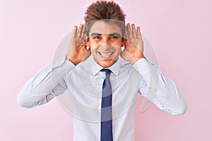 Young handsome businessman wearing shirt and tie standing over isolated pink background Trying to hear both hands on ear gesture,