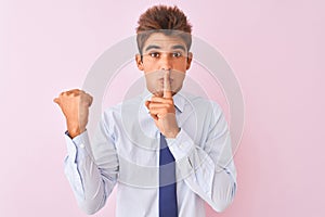 Young handsome businessman wearing shirt and tie standing over  pink background asking to be quiet with finger on lips