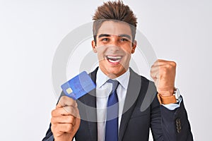 Young handsome businessman wearing suit holding credit card over isolated white background screaming proud and celebrating victory