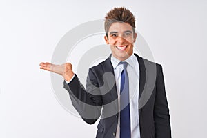 Young handsome businessman wearing suit standing over isolated white background smiling cheerful presenting and pointing with palm
