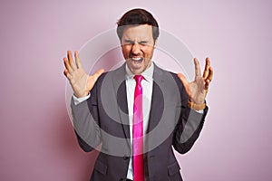Young handsome businessman wearing suit and tie standing over isolated pink background celebrating mad and crazy for success with