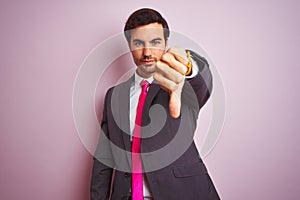 Young handsome businessman wearing suit and tie standing over isolated pink background looking unhappy and angry showing rejection