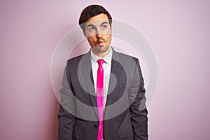 Young handsome businessman wearing suit and tie standing over isolated pink background making fish face with lips, crazy and