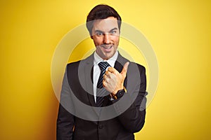 Young handsome businessman wearing suit and tie standing over isolated yellow background doing happy thumbs up gesture with hand