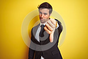 Young handsome businessman wearing suit and tie standing over isolated yellow background looking unhappy and angry showing