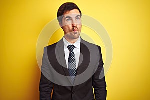 Young handsome businessman wearing suit and tie standing over isolated yellow background making fish face with lips, crazy and